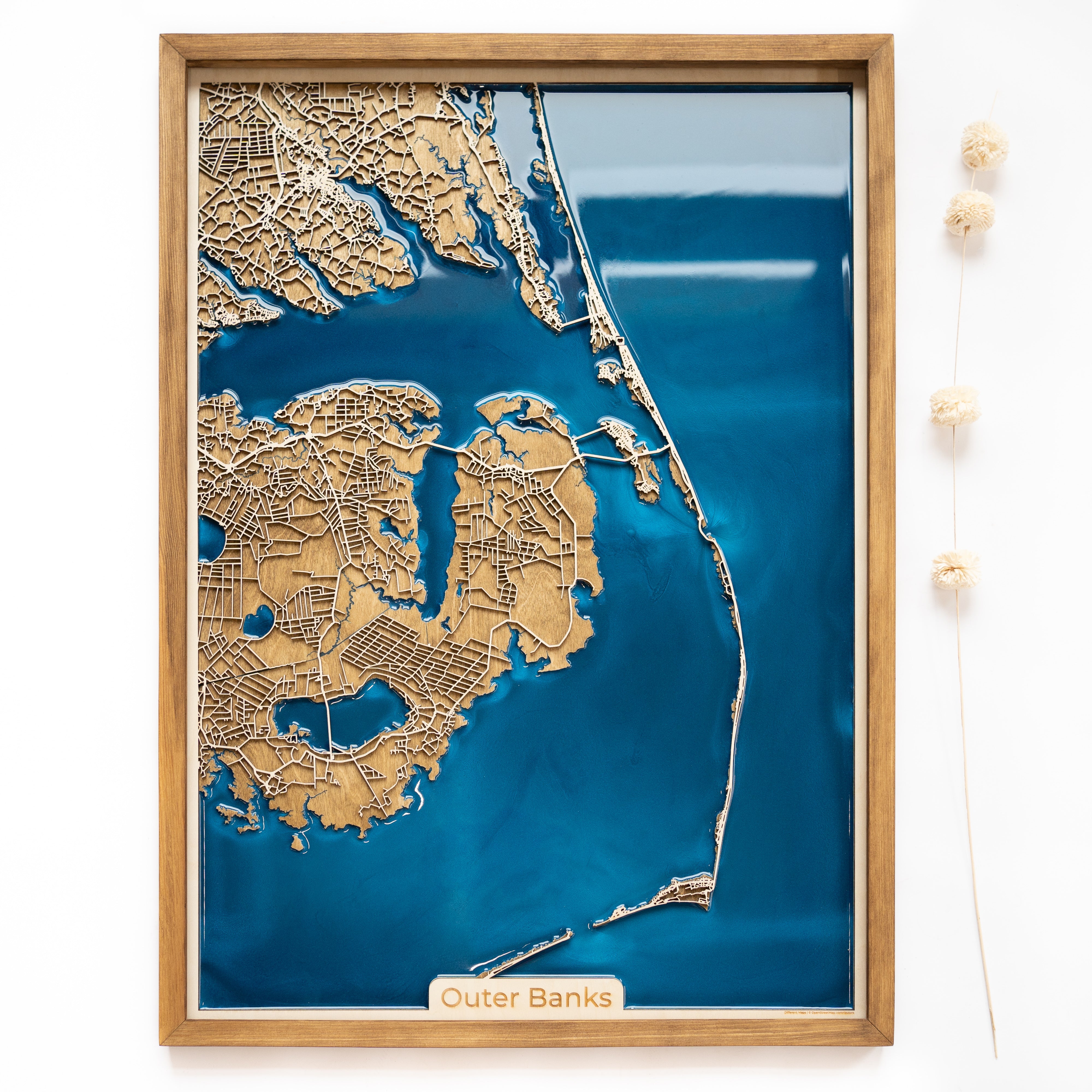 Vertical custom wooden map with epoxy resin of Outer Banks, showcasing intricate details and vibrant blue epoxy in a handcrafted wooden frame.